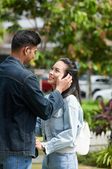 Fototapeta premium Young man touching face of his girlfriend when they are standing in city park and looking at each other
