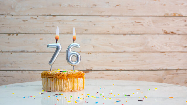 Happy birthday wishes for 76 years from silver numbers on white boards background copy space. Beautiful birthday card with a cupcake with a lit candle for seventy-six years.