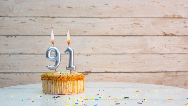91 year happy birthday greetings from silver numbers on white boards background copy space. Beautiful birthday card with a cupcake with a lit candle for ninety one years