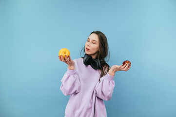 Attractive student girl in headphones around his neck stands on a blue background with apples in his hands.