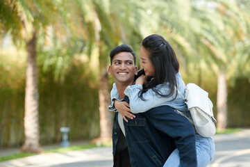 Portrait of smiling young man carrying his cheerful girlfriend when they are spending time in park