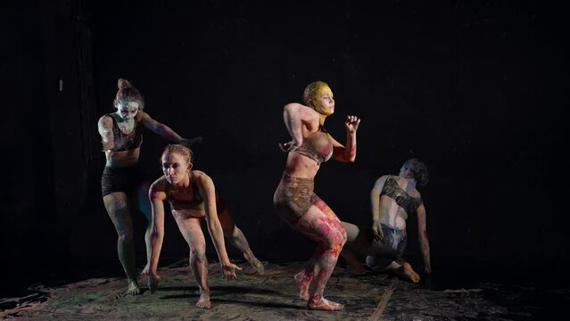 female dancers stained with multicolored paints are dancing in darkness, modern ballet