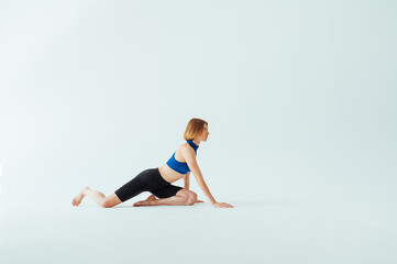 Fototapeta premium Athletic woman warms up before training on a white background, looks to the side while kneeling.