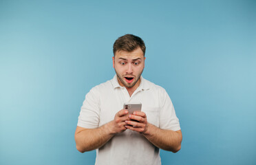 Shocked adult man with bristles looking at smartphone screen with surprised face, isolated on blue background.