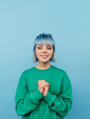 Cute lady in green sweatshirt and colored hair isolated on blue background with smile on face looking at camera.