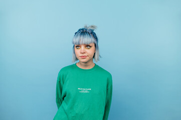 Calm teen girl with bright hair and in a green sweatshirt stands on a snowy background and looks away with a pensive serious face.