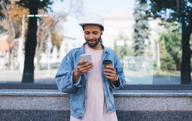 Hispanic hipster guy with caffeine beverage enjoying time for watching online video vlog on mobile...