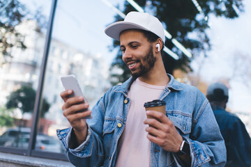 Cheerful Latino hipster guy enjoying free time for watching online video vlog on mobile website,...