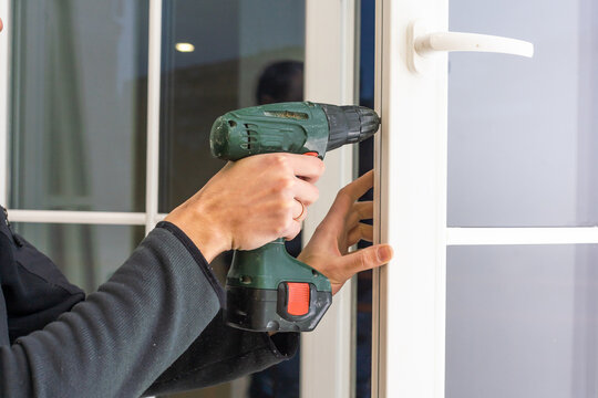 Handsome Man Using A Screwdriver To Install A Window Handle And Looking At The Camera. Making A House Cozy And Warm