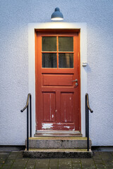 Old worn out red painted wooden door with concrete stairs in front of it