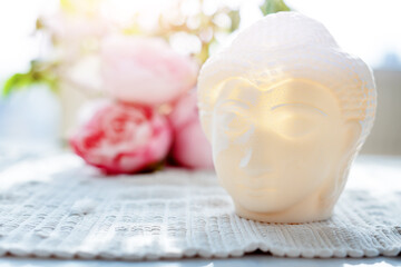 Buddha face. Buddha statue made of white marble with flowers. Concept of peace, meditation, calm and tranquility. Buddhist artifact for Zen style interior decor.