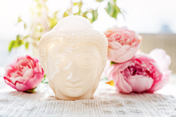 Buddha face. Buddha statue made of white marble with flowers. Concept of peace, meditation, calm and tranquility. Buddhist artifact for Zen style interior decor.