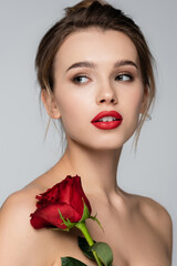 Fototapeta na wymiar young woman with red lips and perfect skin looking away near red rose isolated on grey.