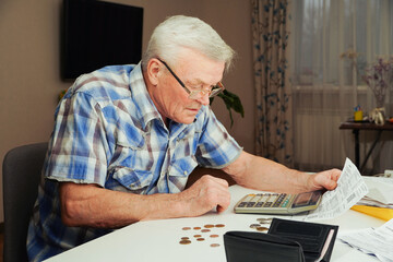 Upset Senior man sitting at the table and calculating finances. Old man checking bills. Man counting coins on the table. Pension calculation concept