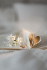 Fototapeta na wymiar Golden ring and open book with folded sheets in heart shape in bed. Wedding concept, Happy Valentine's Day