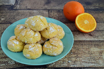 Homemade orange crinkle cookies with powdered sugar icing. Cracked citrus biscuits on wooden background