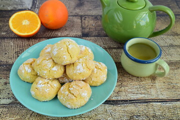 Homemade orange crinkle cookies with powdered sugar icing. Cracked citrus biscuits on wooden background