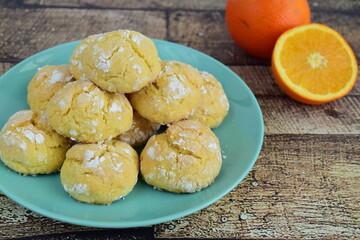 Homemade orange crinkle cookies with powdered sugar icing. Cracked citrus biscuits on wooden background