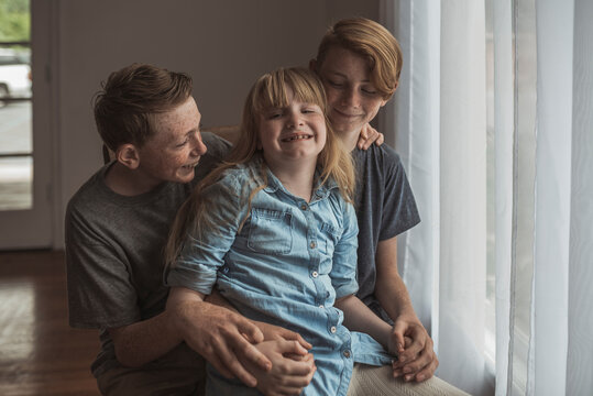 Two brothers and sister sit together in natural light studio