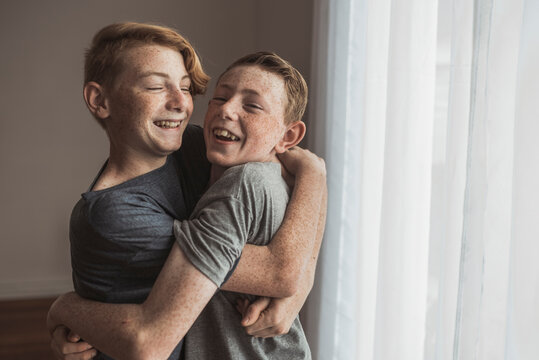Lifestyle portrait of Redhead teen brothers hugging tightly in studio