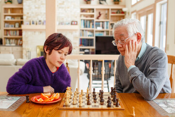 A boy with dyed red hair sits at table with grandfather playing chess