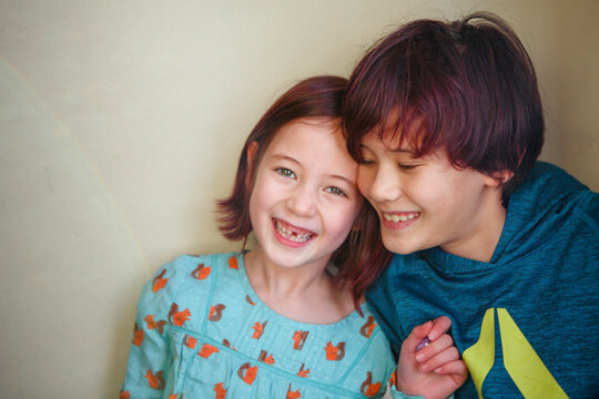 two happy, smiling children lean in close together against a wall