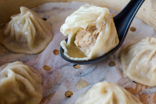 close-up of half-eaten soup dumpling resting on spoon in steam basket