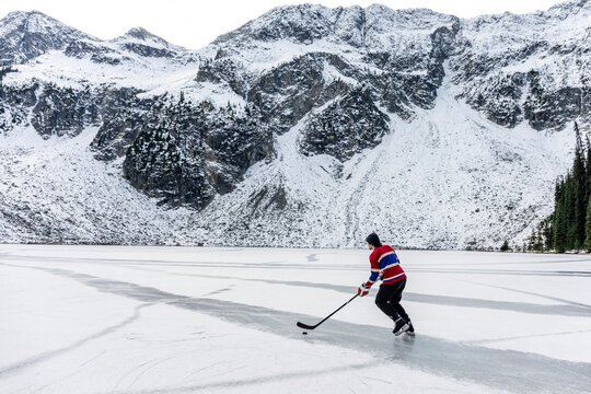 hockey player ice skating on frozen lake near snowy mountain