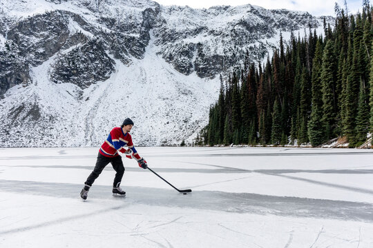 Young man playing ice hockey on lake near snow covered mountain