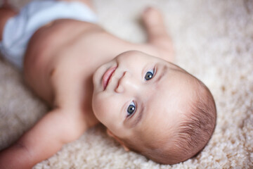 Baby boy laying on carpet and looking at the camera.