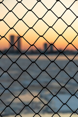 Fototapeta premium Old metal fence with a colorful sunset and Riga city in the background. Andrejosta pier by the harbour.
