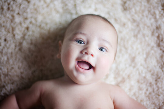 Baby boy laying on carpet and looking at the camera and smiling.