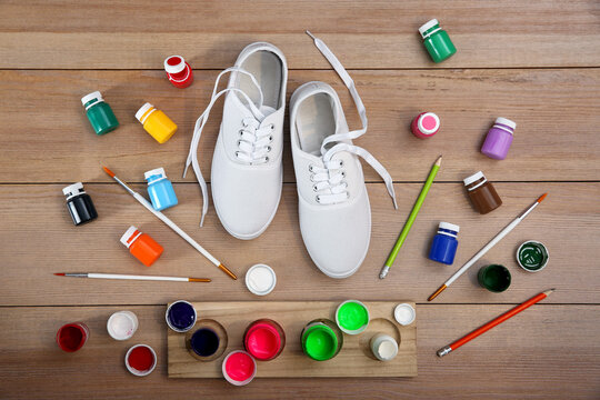 White sneakers and painting supplies on wooden table, flat lay. Customized shoes