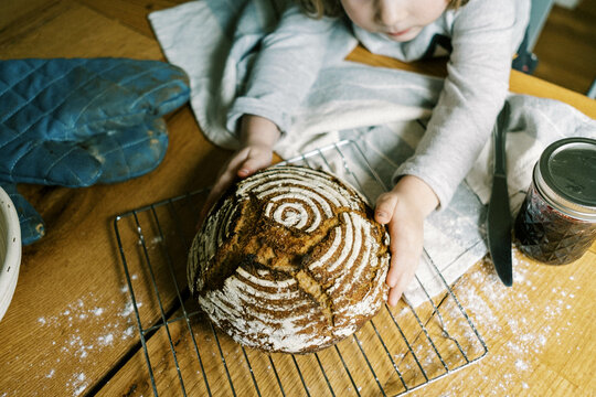 little toddler girl and a fresh sourdough bread at the kitchen table