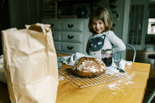 little toddler girl and a fresh sourdough bread at the kitchen table
