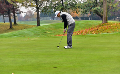 A golfer on the green evaluates the slopes and distance to the hole before aiming the ball towards...