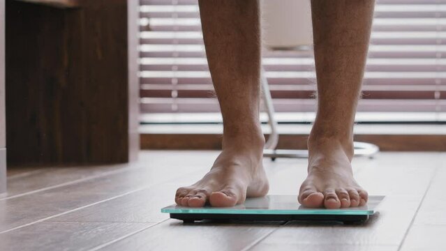 Close-up male legs slender thin sporty unrecognizable guy male athlete standing at home bathroom walking barefoot on electronic scales checking weight slimming body control kilograms sports fattening