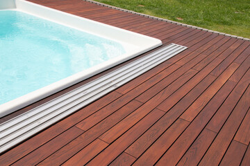 Teak wood pool deck, decking installed around the blue swimming pool