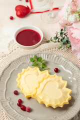 Romantic breakfast for Valentine's Day. Cheesecakes in the shape of a heart, decorated with berries and mint. Glasses, flowers and hearts in the background.