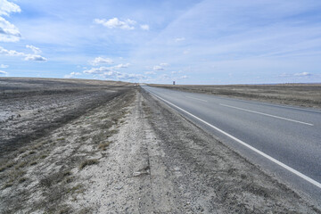 Naklejka premium Highway road in the steppes, bushes, grass and cloudy sky. Spring.