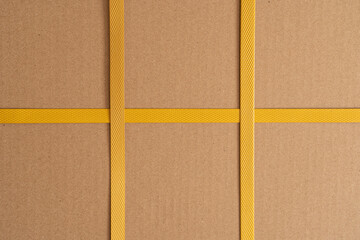 Brown cardboard box tied with yellow strapping tape. There are two crossings of the tape....