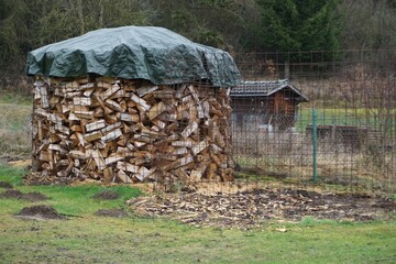 Gartenlandschaft mit Brennholzlager hinter Draht, Wiese, Zaun und kleinem alten Holzschuppen vor...