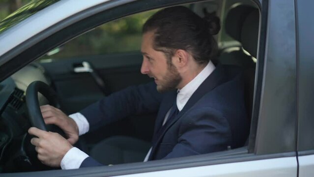 Side view irritated nervous male Caucasian driver pushing horn on steering wheel driving in traffic jam in sunbeam outdoors. Portrait of annoyed angry man on driver's seat in car