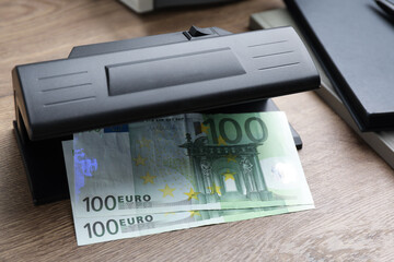 Modern currency detector with Euro banknotes on wooden table. Money examination device