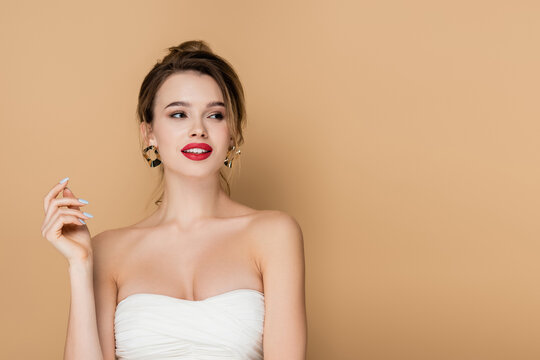 smiling woman in strapless top and makeup looking away isolated on beige.