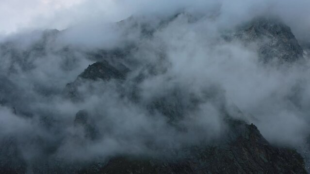 Dense clouds around rocky black mountain peaks. Twilight atmospheric landscape of dark rocks and fog