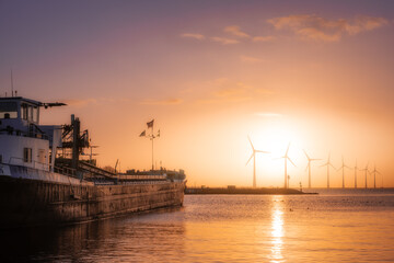 A ship with cargo sails past windmills to sunrise on the Ijsselmeer in the Netherlands - obrazy, fototapety, plakaty