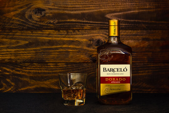 A bottle of Ron Barcelo Dominican rum, Dorado Anejado and a glass with ice on a dark wooden background. Ron Barcelo mild Caribbean rum is made from sugar cane juice and aged in American oak barrels