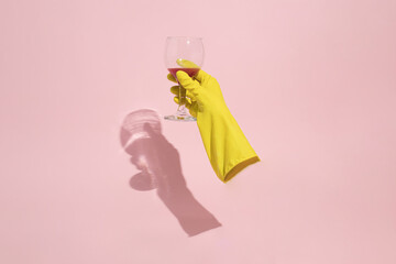 A hygienic glove holds a glass of wine on a pink background. Minimal lay out composition.