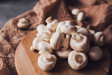 Fresh white champignons on a cutting board on a brown textile background. Kitchen, cooking, recipes. Mushrooms, ingredient